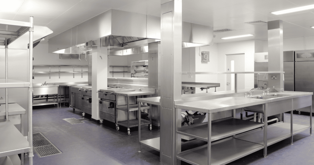 An image of a stainless steel commercial kitchen with overhead task lighting ti brightly illuminate the surfaces
