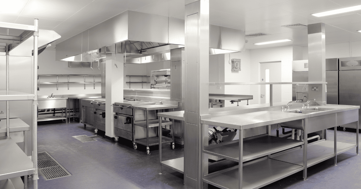 An image of a stainless steel commercial kitchen with overhead task lighting ti brightly illuminate the surfaces